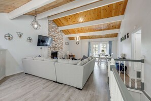 A modern living room with a sectional sofa, a TV, a fireplace, and a staircase leading to another level. - Gateway to Big Bear! High-Country Home w/ Deck (Running Springs)