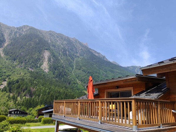 Une cabane en bois dotée d’une terrasse, entourée d’une végétation luxuriante et de montagnes.