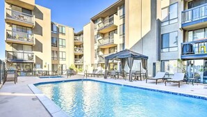 Une piscine entourée de bâtiments à plusieurs étages dotés de balcons, avec des chaises longues et des parasols à proximité.