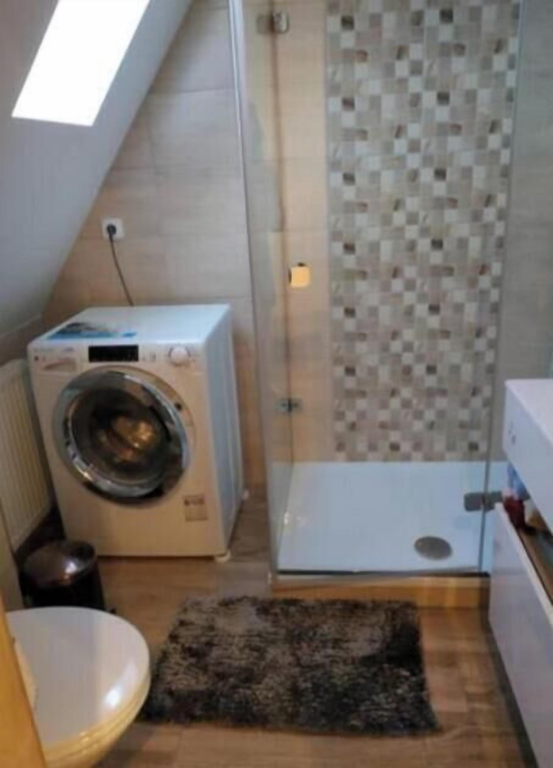 Casa de banho compacta com máquina de lavar roupa, cabine de duche e um tapete pequeno.