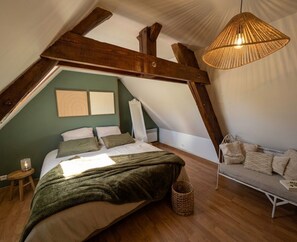 A bedroom with a sloped ceiling, a bed, a hanging light fixture, a bench, and a wall-mounted artwork. - L'Aparté Percheronne in La Perrière (La perriere)