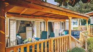 A wooden deck with a covered seating area, a table with items, and a view of a house in the background. - Comfort Plus Stay by Adriatic for 7 (Brtonigla)