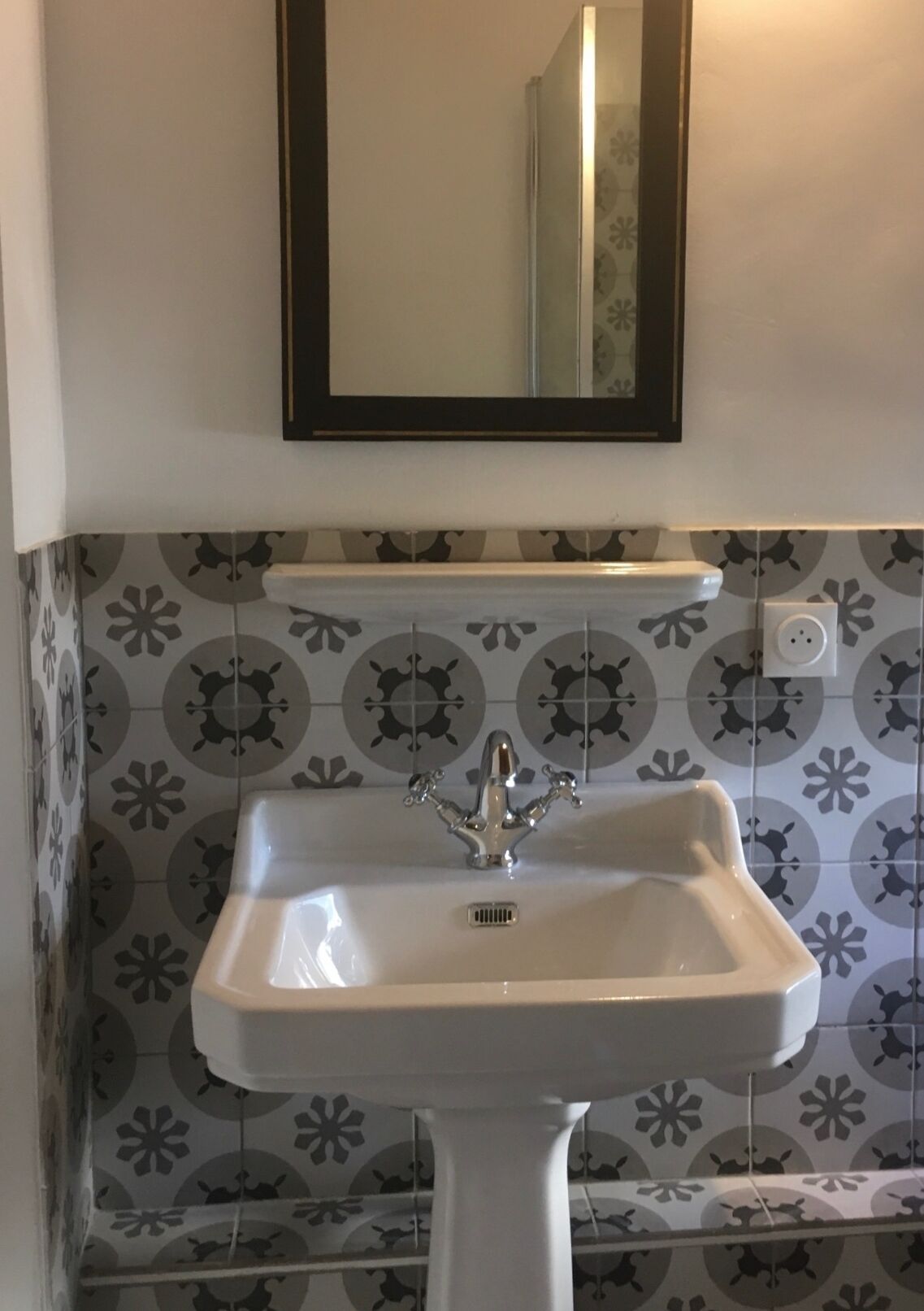 A bathroom with a white pedestal sink, a mirror above it, and patterned tiles on the walls.