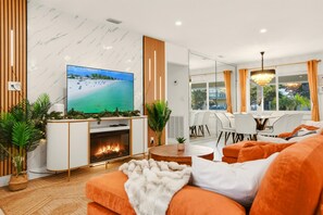 Ein modernes Wohnzimmer mit Kamin, Fernseher und Essbereich mit Blick ins Freie.