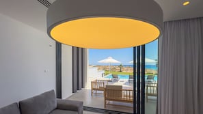 A modern interior with a large window, a sofa, and a view of a pool and beach. - Aqua Beachfront Villas #1, Aqua Beachfront Villas - Villa 1 (Ayia Napa)