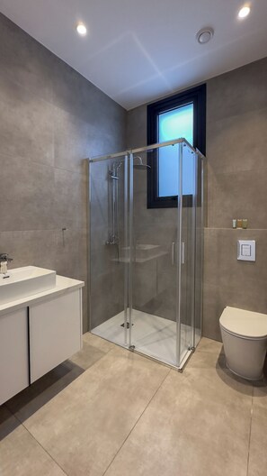 Un baño moderno con ducha acristalada, lavabo blanco y retrete.