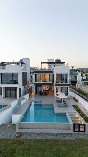 Un moderno edificio residencial de varios pisos con un patio central, mobiliario exterior y una piscina.