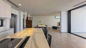 A modern kitchen with a marble countertop, pendant lighting, and a dining area with a wooden table and chairs.