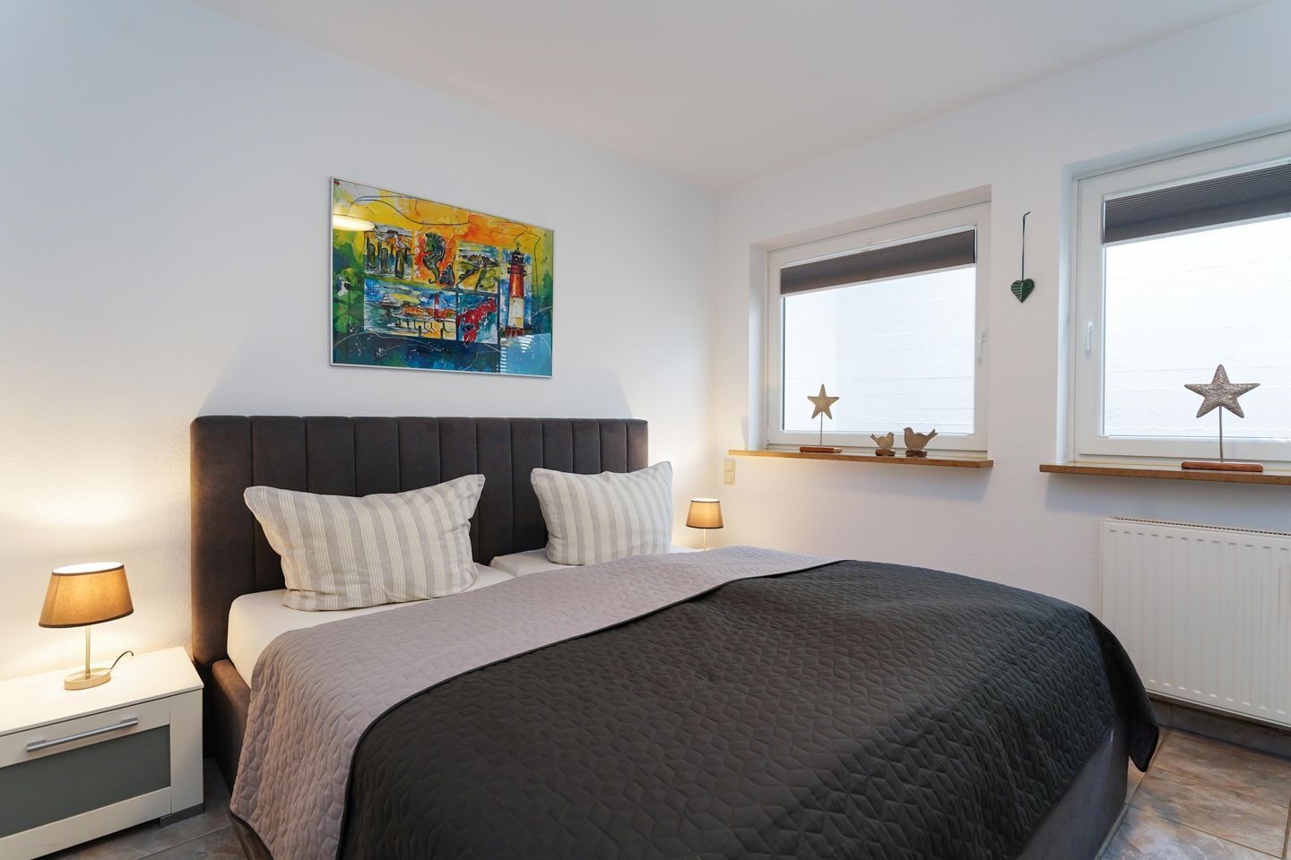 Une chambre à coucher avec un lit, des lampes de chevet, une fenêtre décorée d’étoiles et un tableau coloré accroché au mur.