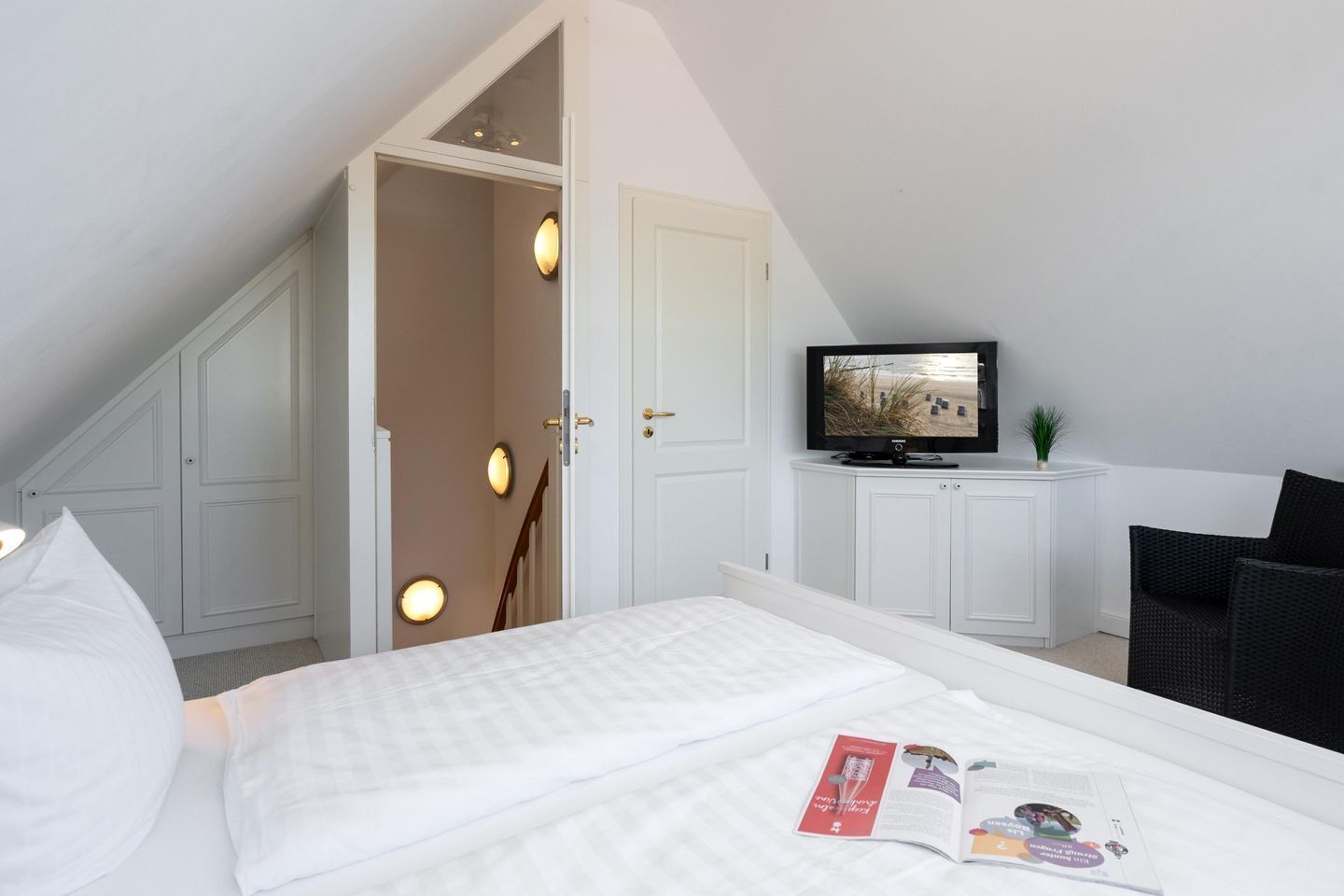 A bedroom with a bed, a TV, a chair, and a door leading to a balcony.