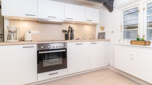 Una cocina moderna con armarios blancos, horno empotrado, cafetera y ventana con vistas.