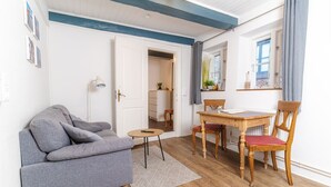 A living room with a grey sofa, a wooden dining table with chairs, a small round table, and a door leading to another room. - fewo1846 - Matrosenkoje - fewo1846 - Matrosenkoje - centrally located (Flensburg)