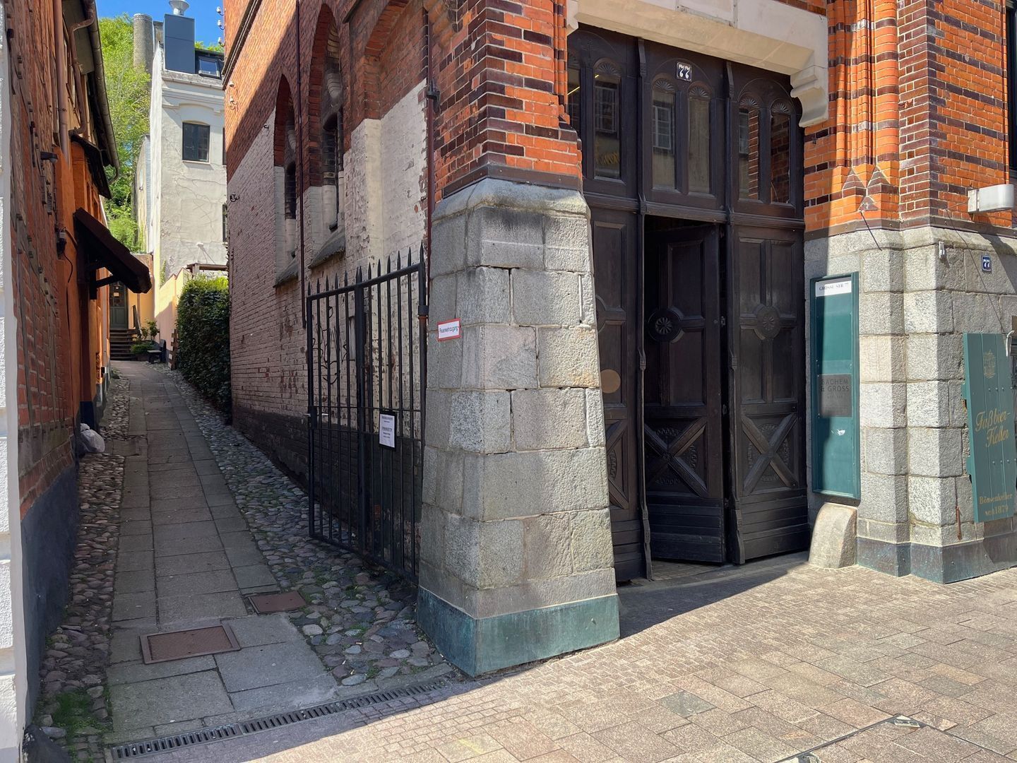 A narrow alley with a brick building, a metal gate, and a stone pillar.
