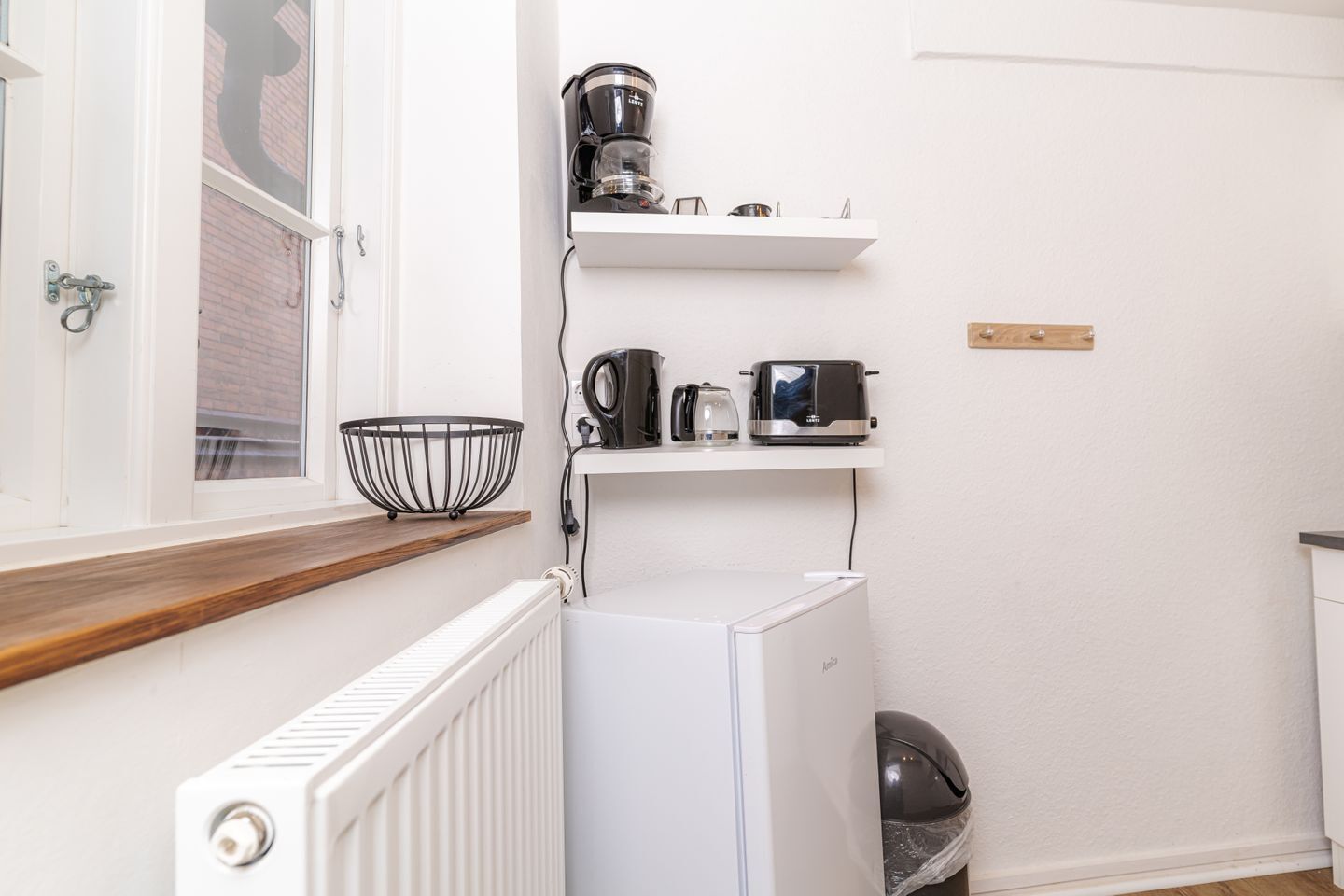 Una cocina compacta con un refrigerador blanco, una cafetera, un hervidor y una tostadora sobre un estante blanco.