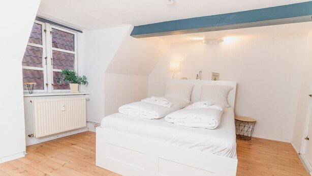 A bedroom with a bed, a radiator, a window with a plant, and a bedside table. - fewo1846 - Sternkoje - fewo1846 - Sternkoje - ideal for a relaxing time out (Flensburg)