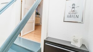A staircase with a blue handrail leading to a room with a white wall and a framed picture of a lighthouse with the text 'HEIMAT HABEN'. - fewo1846 - Sternkoje - fewo1846 - Sternkoje - ideal for a relaxing time out (Flensburg)