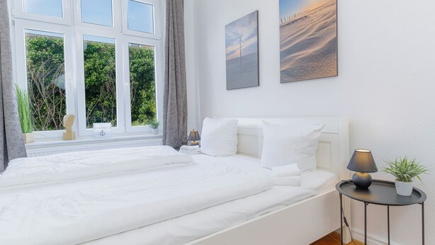 Ein Schlafzimmer mit einem großen Bett, einem Nachttisch mit Lampe und zwei an der Wand hängenden Bildern.
