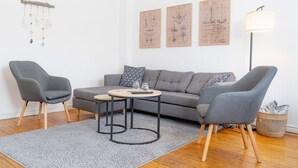 Ein modernes Wohnzimmer mit grauem Sofa, zwei Sesseln, einem Couchtisch und einer Lampe.