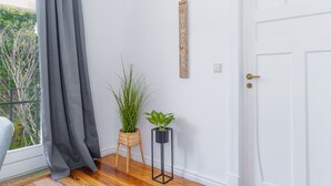 Ein Zimmer mit weißer Tür, grauem Vorhang, einem Holunderschild und zwei Blumentöpfen.