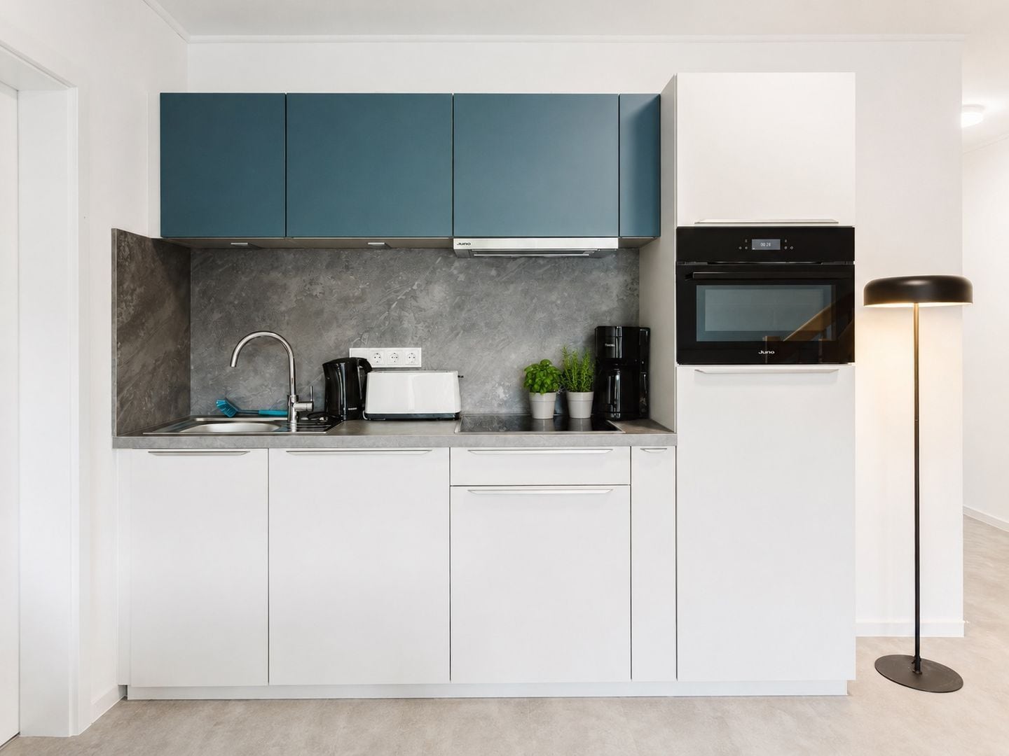 Una cucina moderna con mobili bianchi, un forno nero, una macchina da caffè e un tostapane.