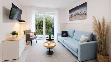 Ein modernes Wohnzimmer mit Sofa, Couchtisch, Fernseher und einem Balkon mit Pflanzen.