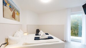 Hotellihuone, jossa on sänky, tyynyjä, sängynpääty, taulu seinällä ja parveke, jossa on kaide.