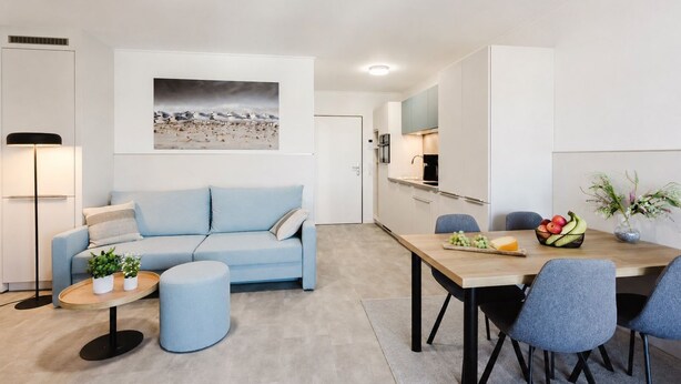 A modern living room with a sofa, a coffee table, and a dining area with chairs and a table set for two. - MEERholung FeWo 4.10 - Exclusive penthouse with sea view & roof terrace flair - (Cuxhaven)