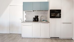 A compact kitchen with a built-in oven, a coffee maker, and a sink. - MEERholung Vacation Rental 4.8 – Modern Penthouse, Close to the Beach, with Ocean View - House (Cuxhaven)
