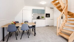 A modern kitchen with white cabinets, a wooden staircase, and a dining area with a table and chairs. - MEERholung Vacation Rental 4.8 – Modern Penthouse, Close to the Beach, with Ocean View - House (Cuxhaven)