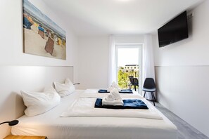 A hotel room with a bed, a TV, a painting, and a view of buildings. - MEERholung Vacation Rental 1.3 with Balcony Near the Beach, Sleeps Up to 4 - MEERholung House (Cuxhaven)