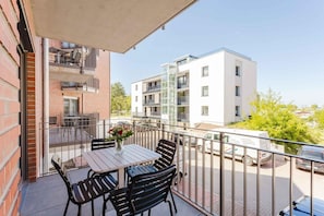 A balcony with a table and chairs, a vase with flowers, and a view of adjacent buildings. - MEERholung Vacation Rental 1.9 Near the Beach with Balcony for Up to 4 People - MEERholung House (Cuxhaven)