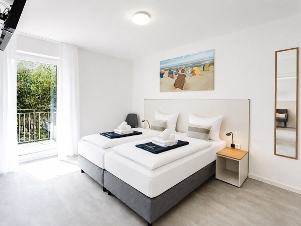 Ein modernes Hotelzimmer mit großem Fenster, zwei Betten, einem Gemälde, einem Nachttisch und einem Sessel.