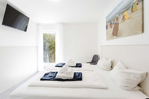 A hotel room with a bed, a chair, a TV, and a painting. - MEERholung Vacation Rental 1.4 with a balcony and within walking distance of the beach, for 4 people - House (Cuxhaven)