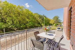 Ein Balkon mit Tisch und Stühlen, einer Blumenvase und Blick auf Bäume und eine Straße.