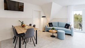 En moderne stue med spisebord, grå stole, en blå sofa og et rundt bord med en plante.