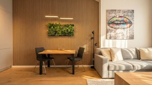 A modern room with a wooden slat wall, a dining table with chairs, a sofa, a floor lamp, and a wall art piece. - 8-Min to Airport 1BR & 1LR Flat (Bratislava)