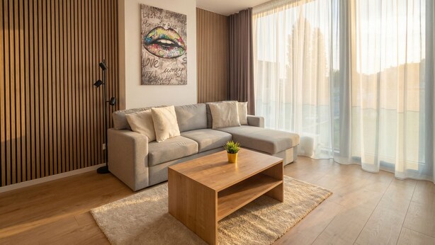 A modern living room with a sofa, a coffee table, and a large window with sheer curtains. - 8-Min to Airport 1BR & 1LR Flat (Bratislava)