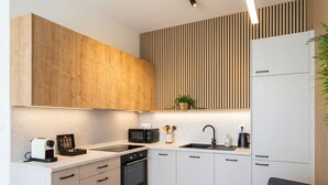 A modern kitchen with wooden cabinets, a microwave, a sink, and a dining area with a table and chair. - 8-Min to Airport 1BR & 1LR Flat (Bratislava)
