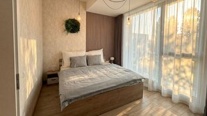 A bedroom with a bed, a nightstand, a wall-mounted plant, and a window with sheer curtains. - 8-Min to Airport 1BR & 1LR Flat (Bratislava)