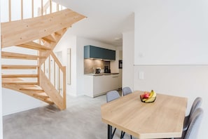 A modern kitchen with white cabinets and a blue accent wall, a wooden staircase, and a dining area with a fruit bowl on the table. - MEERholung Vacation Rental 4.6 – Beachfront Penthouse for up to 7 People with a Balcony - (Cuxhaven)