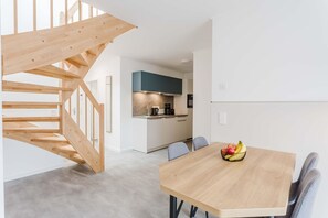 A modern kitchen with white cabinets and a blue accent wall, a wooden staircase, and a dining area with a fruit bowl on the table. - MEERholung Vacation Rental 4.6 – Beachfront Penthouse for up to 5 People with a Balcony - House (Cuxhaven)