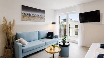 Ein modernes Wohnzimmer mit einer Couch, einem Couchtisch, einer Zimmerpflanze und einem Fernseher.