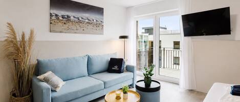 Una sala de estar moderna con un sofá, una mesa de centro, una planta en maceta y un televisor.