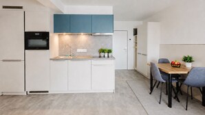 Cuina moderna amb armaris blancs, una secció superior blava i zona de dinar amb taula i cadires de fusta.