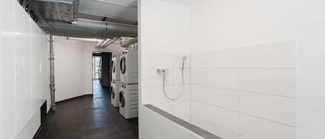 A laundry room with stacked washers and dryers, a shower, and a ventilation system.