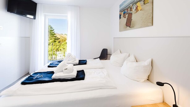 Habitación de hotel con cama, televisor montado en la pared, un cuadro y vistas al exterior.