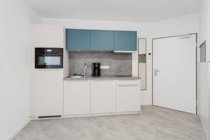A compact kitchen with white cabinets, a black oven, a coffee maker, and a teal upper cabinet. - MEERholung Vacation Rental 2.1: Beachfront Studio Near the Forest - MEERholung House (Cuxhaven)