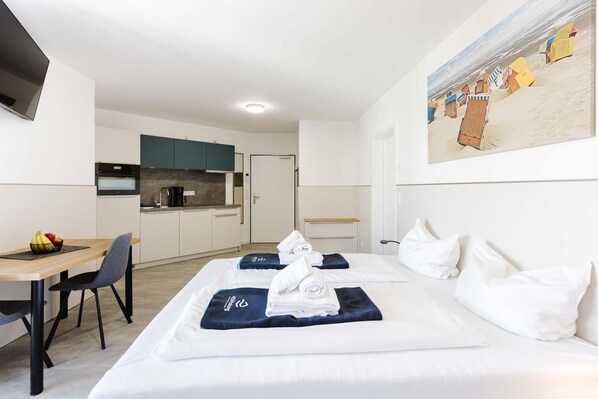 A hotel room with a bed, a desk, a chair, a kitchen area, and a painting on the wall. - MEERholung Vacation Rental 2.1: Beachfront Studio Near the Forest - MEERholung House (Cuxhaven)