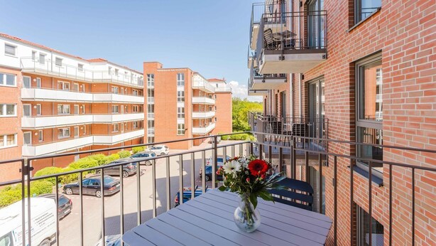Een balkon met een witte tafel, een vaas met bloemen en een uitzicht op meerverdiepinggebouwen.