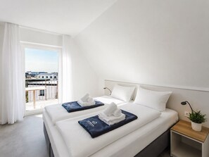 Quarto de hotel com duas camas, varanda, vista para prédios e uma pequena mesa de cabeceira com uma planta.